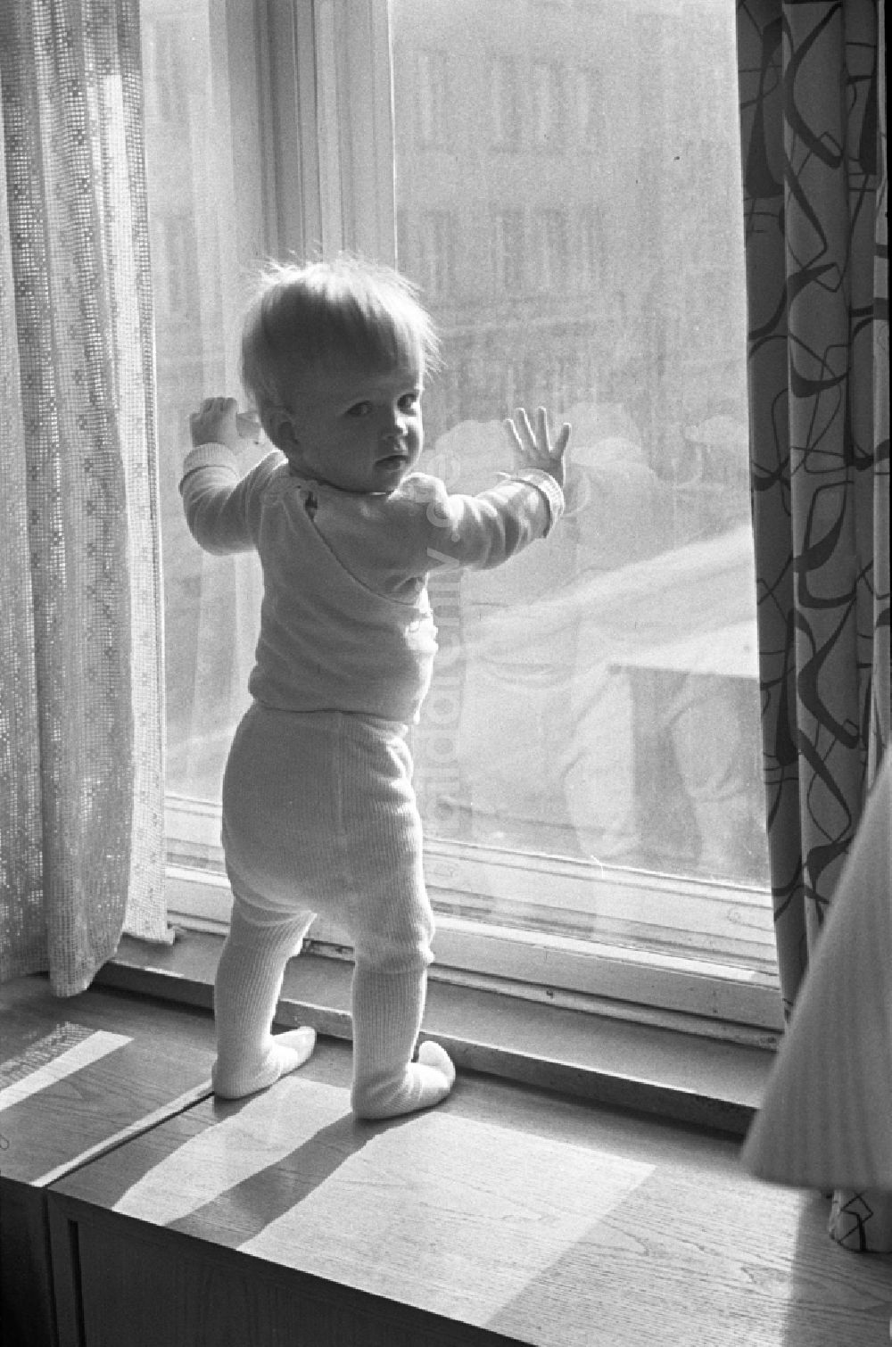 DDR-Fotoarchiv: Berlin - Friedrichshain - Ein kleines Kind mit Strumpfhosen steht auf der Fensterbank in Berlin